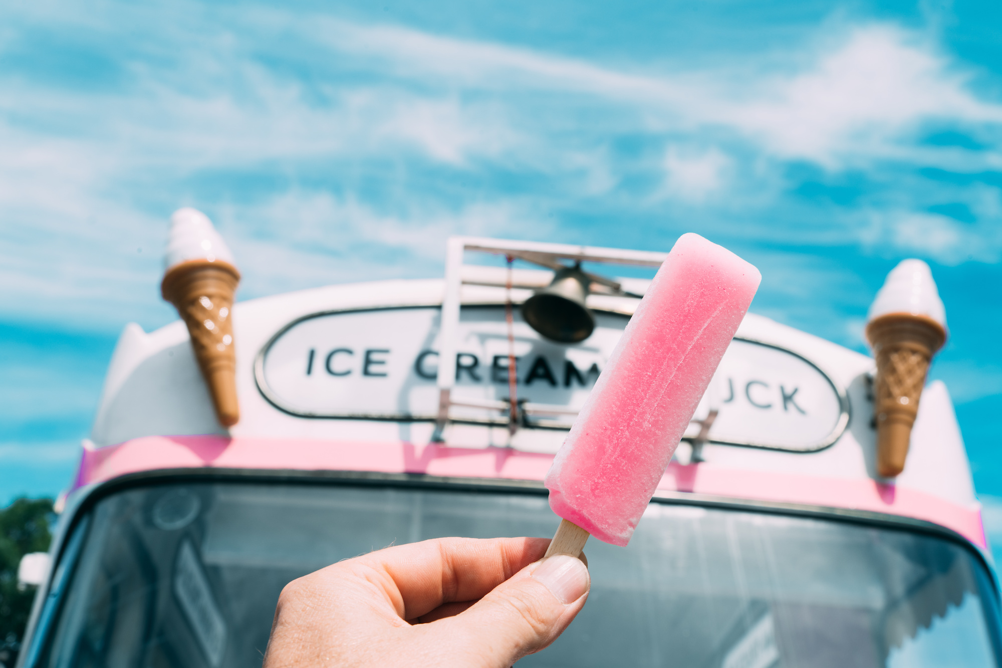 Pink ice cream with a pink ice cream truck or van in the background. Hand holding ice cream.